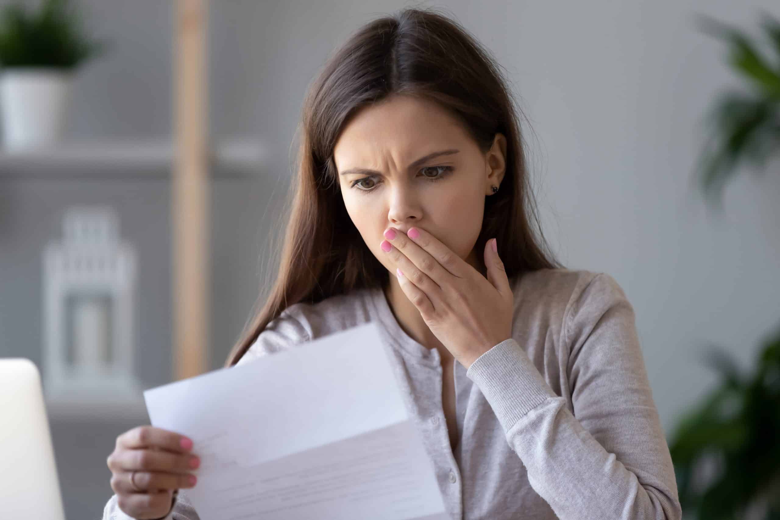 Shocked stressed young woman reading document letter from bank about loan debt financial problem